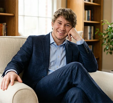 Woody Mabbott, Founder of Creator Connect, smiling while leaning on a sofa, featured in a client review for Prox Digital Agency. He wears a blue plaid suit jacket and a light blue dress shirt against a background of bookshelves.